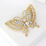 Butterfly brooch with gold-tone finish, clear faceted stones, and openwork wing design, angled top view on white in studio.