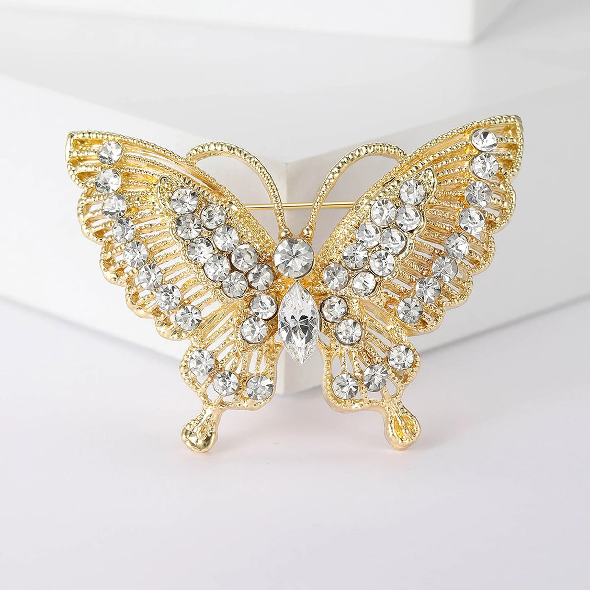 Butterfly brooch with gold-tone metal base, clear round and marquise-cut stones, front view on white block.