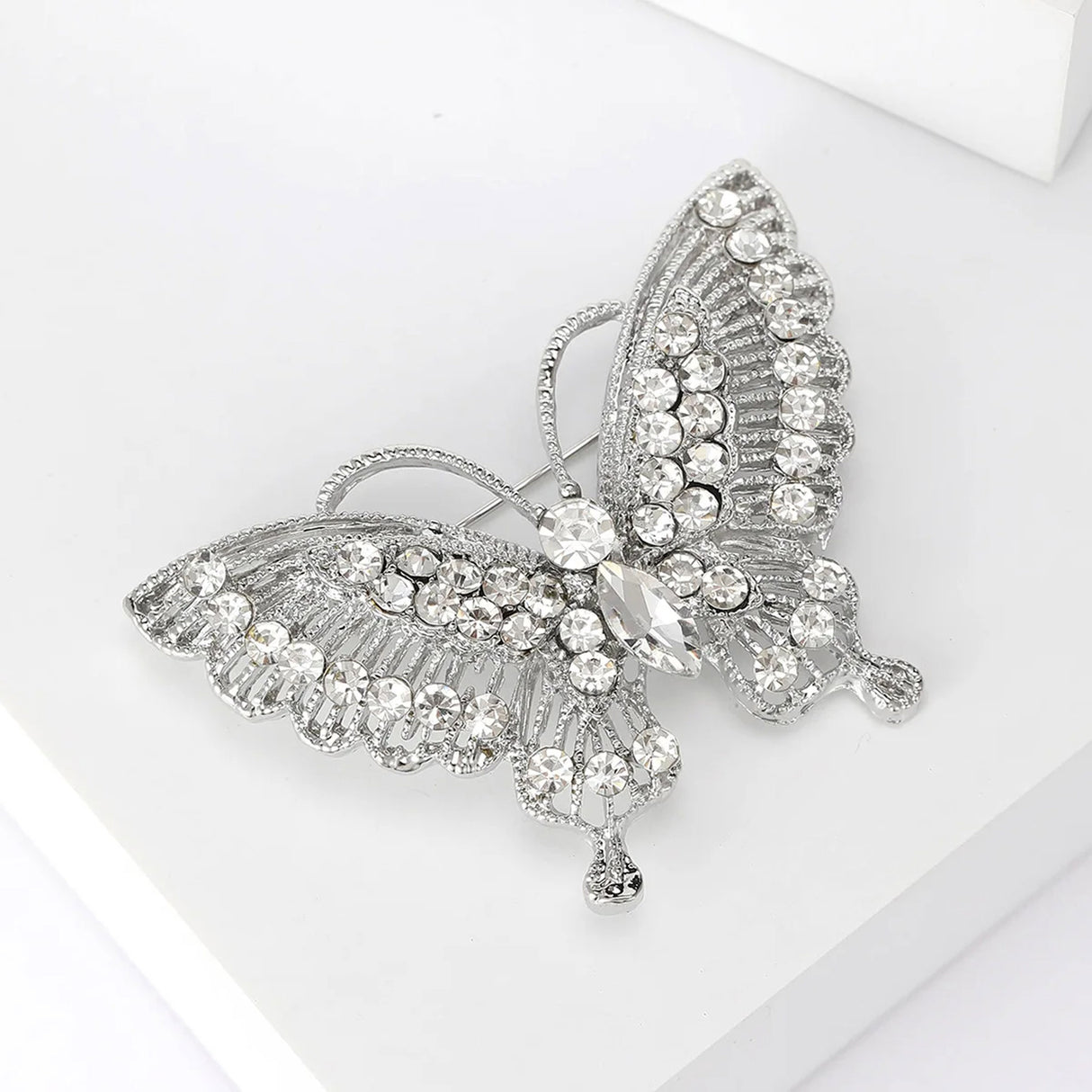Butterfly brooch in silver-tone metal with clear round stones and marquise center stone, angled view on white.