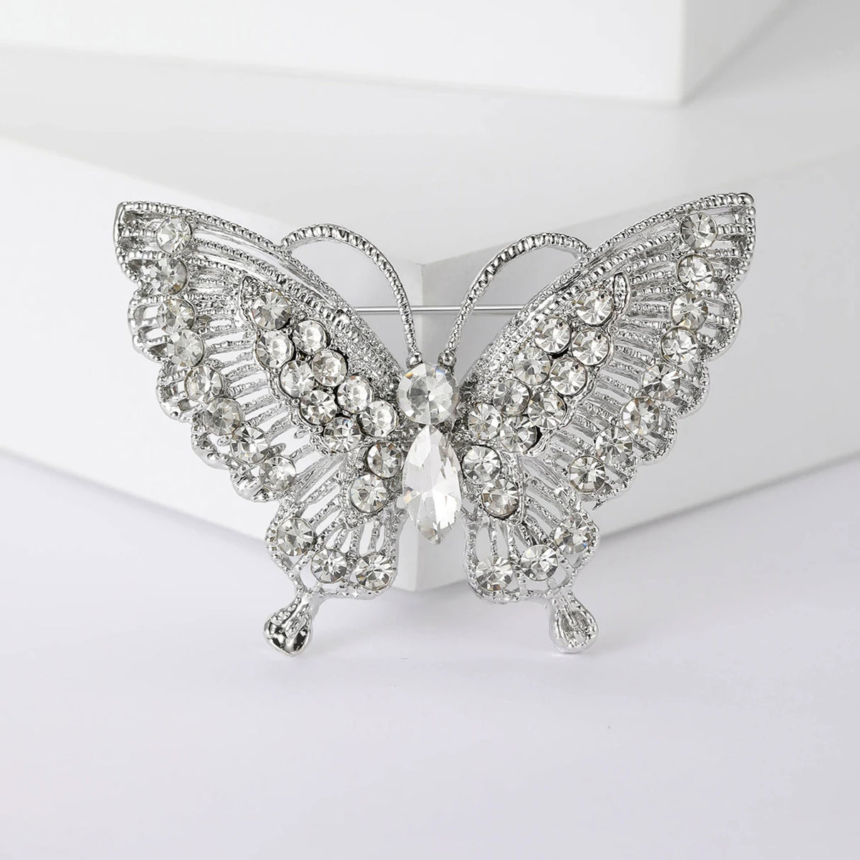 Butterfly brooch with silver-tone metal base, clear faceted stones and intricate cutout wings, front view on white block.