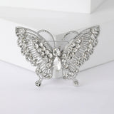 Butterfly brooch with silver-tone metal base, clear faceted stones and intricate cutout wings, front view on white block.