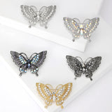 Set of five butterfly brooches in assorted silver, gold, and black tones with clear, iridescent, and dark stones, flat lay on white.
