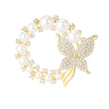 Butterfly brooch with gold-tone metal, round white faux pearls, and clear faceted stones in circular design, cutout on white.