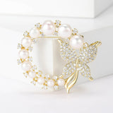Butterfly brooch in gold-tone metal with white round beads and clustered clear stones, standing on white block.