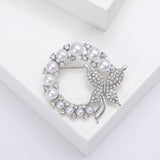 Butterfly brooch with silver-tone metal, glossy white round beads, and clear faceted stones, flat lay on white block.