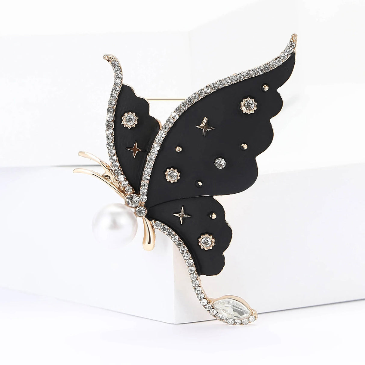 Butterfly brooch with black wings, clear faceted stones, pearl accent, and star motifs, front view on white block in studio.