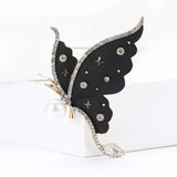 Butterfly brooch with black wings, clear faceted stones, pearl accent, and star motifs, front view on white block in studio.