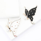Set of two butterfly brooches with white and black wings, clear and pink stones, and pearl details, flat lay on white surface.