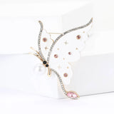 Butterfly brooch with white-tone wings, pink stones, pearl body, and star motifs, upright pose on white block.