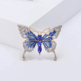 Butterfly brooch with deep blue and white enamel wings, gold-tone outline, clear decorative stones, and vertical row of blue faceted oval stones at center, upright pose on white.