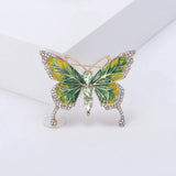 Butterfly brooch featuring green and yellow enamel wings, gold-tone trim, clear wing stones, and three green faceted oval stones at center, upright pose on white block.