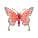 Butterfly brooch with coral-pink enamel wings, gold-tone metal base, small clear round stones along edges, and three large pink faceted stones forming the body. Cutout on white.
