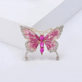 Butterfly brooch with pink enamel wings trimmed in gold-tone metal, clear decorative stones, and three pink faceted ovals vertically aligned as body. Upright view on white in studio setting.