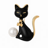 Cat brooch with black enamel body, gold-tone accents, white round faux pearl, and bow detail, cutout on white background.