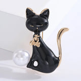 Cat brooch featuring black enamel body, gold-tone accents, and a white round bead, upright pose on white studio platform.