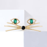 Cat face brooch in gold-tone with green oval stones for eyes and black round nose, displayed on white block.