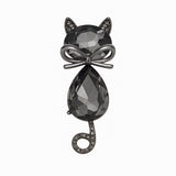 Cat brooch with black faceted stones, gunmetal-tone bow detail, and curled tail with clear stones, cutout on white.
