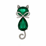 Cat brooch with green faceted stones, silver-tone bow detail, and spiral tail adorned with clear stones, cutout on white.