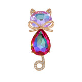 Cat brooch with iridescent pink-purple faceted stones, gold-tone bow accent, and curled tail with clear stones, cutout on white.