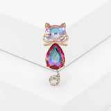 Cat brooch with iridescent pink faceted stones, gold-tone bow detail, and curled tail with clear stones, upright pose on white studio backdrop.
