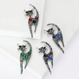 Set of four cat brooches with antique-style silver-tone outlines and multicolor faceted stones, arranged on layered white platforms in studio.
