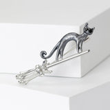 Cat brooch with gray-tone body positioned on silver-tone broomstick with faceted stones, front studio view on white block.