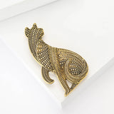 Cat brooch in gold-tone metal with textured geometric detailing, angled flat lay on white platform.