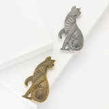 Pair of cat brooches in gold-tone and silver-tone metal finishes with geometric textures, flat lay on white surface.
