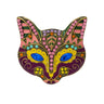 Cat mask brooch with blue faceted eyes and multicolor enamel and stones. Main enamel colors include yellow and purple, stones include pink and blue. Cutout on white background.