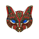 Cat brooch with red-brown enamel, blue faceted eyes, green and white accents, cutout on white background.