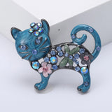 Cat brooch with blue enamel finish, blue and pink stones, floral accents, and green leaf detail, angled view.