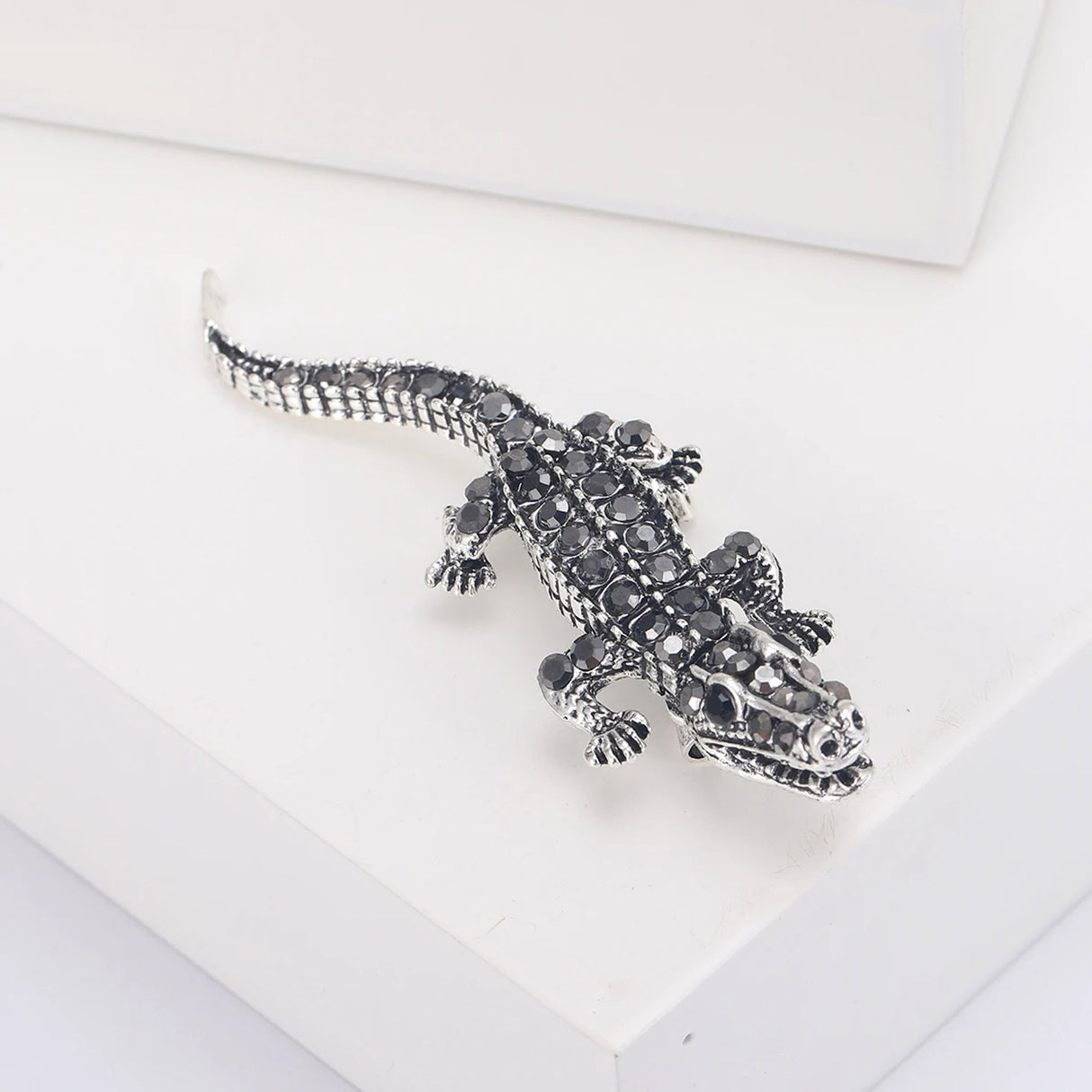 Crocodile brooch with silver-tone metal and black faceted stones, angled front view on white studio platform.