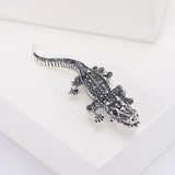 Crocodile brooch with silver-tone metal and black faceted stones, angled front view on white studio platform.