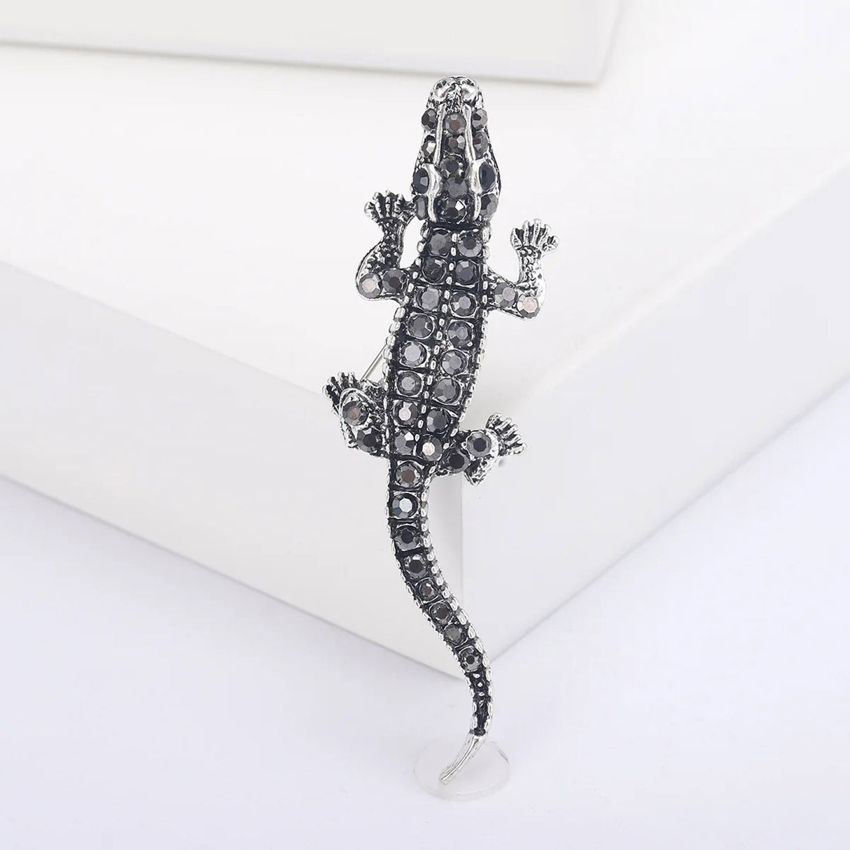 Crocodile brooch featuring silver-tone metal and black faceted stones, upright display on white platform.