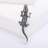 Crocodile brooch featuring silver-tone metal and black faceted stones, upright display on white platform.