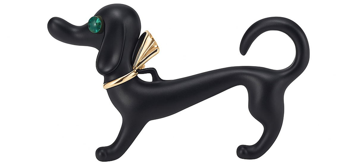Dachshund dog brooch with matte black finish, green faceted eye, and gold-tone bow accent, cutout on white background. Landscape crop for secondary use.