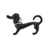 Dachshund dog brooch with matte black finish, green faceted eye, and gold-tone bow accent, cutout on white background.