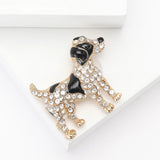 Dog brooch with gold-tone base metal, black enamel patches, and clear faceted stones. Angled top-down view on white studio surface.