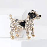 Dog brooch with black enamel details, gold-tone metal, and clear decorative stones, upright pose on white block.