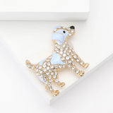 Dog brooch with light blue enamel patches, clear faceted stones, and gold-tone outline. Angled bird's eye view on white background in studio.
