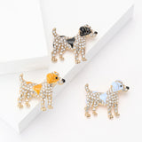 Trio of dog brooches with black, yellow, and light blue enamel patches, gold-tone base metal, and clear stones. Studio flat lay on white backdrop.