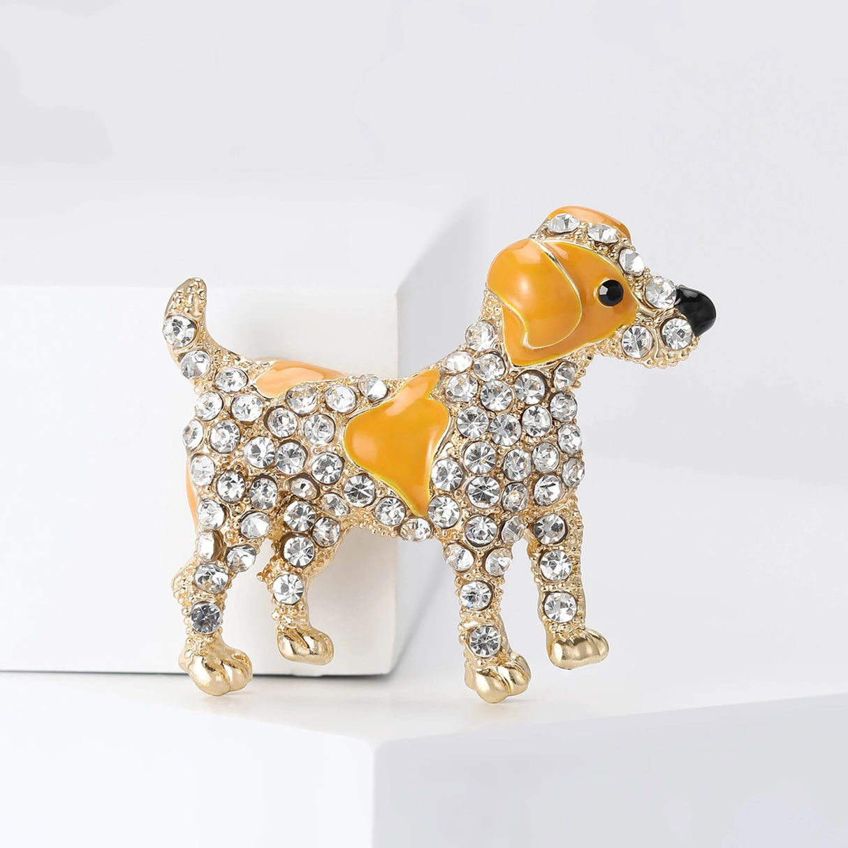 Dog brooch with yellow-orange enamel accents, gold-tone finish, and clear faceted stones, upright studio view on white block.