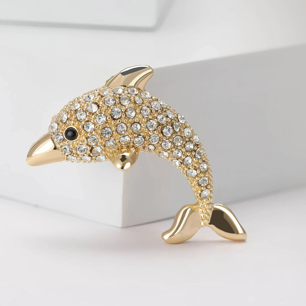 Dolphin brooch in gold-tone with clear faceted stones and black eye detail, upright position on white studio background.
