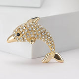 Dolphin brooch in gold-tone with clear faceted stones and black eye detail, upright position on white studio background.