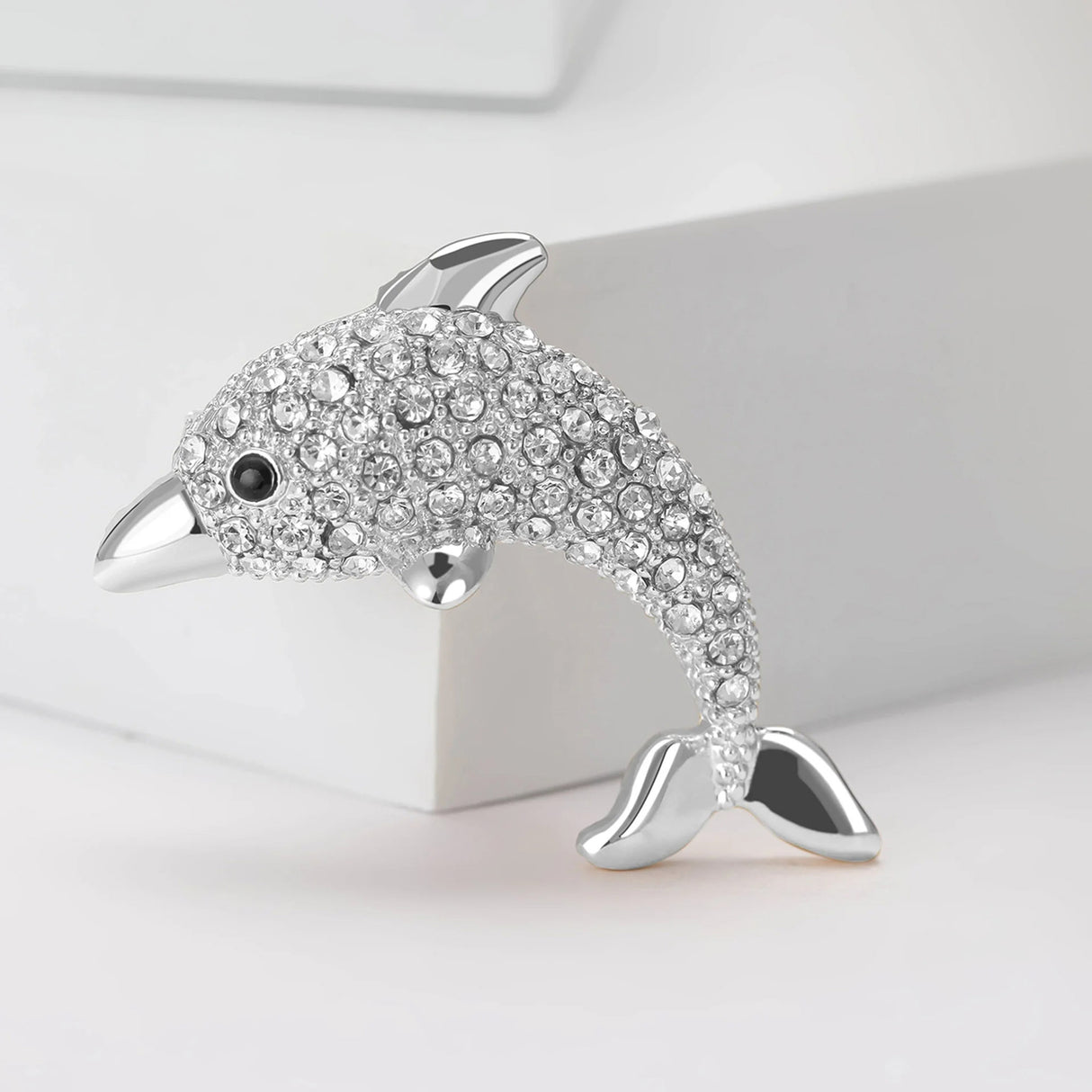 Dolphin brooch in silver-tone metal with clear faceted stones and black eye detail, upright pose on white.