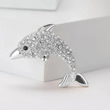Dolphin brooch in silver-tone metal with clear faceted stones and black eye detail, upright pose on white.