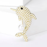 Dolphin brooch with gold-tone base, white round beads, black eye detail, and a single large faux pearl, upright pose on white studio backdrop.