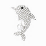 Dolphin brooch with silver-tone metal finish, covered in small white round beads, black eye detail, and suspended imitation pearl, cutout on white background.