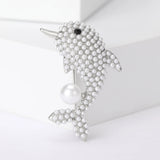 Dolphin brooch with silver-tone metal base, small white round beads, black eye accent, and a large imitation pearl, upright pose on white studio background.