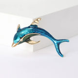 Dolphin brooch featuring a glossy blue body with gold-tone details, displayed upright on white studio platform.